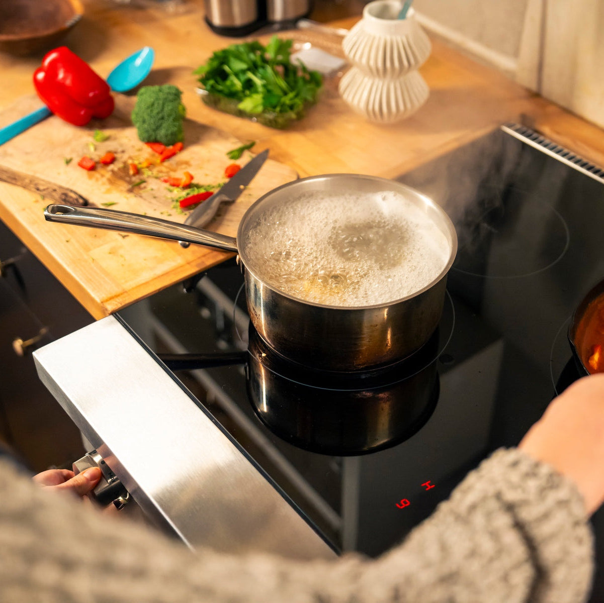 Person cooking on a stovetop with a pot boiling and another dish being stirred.